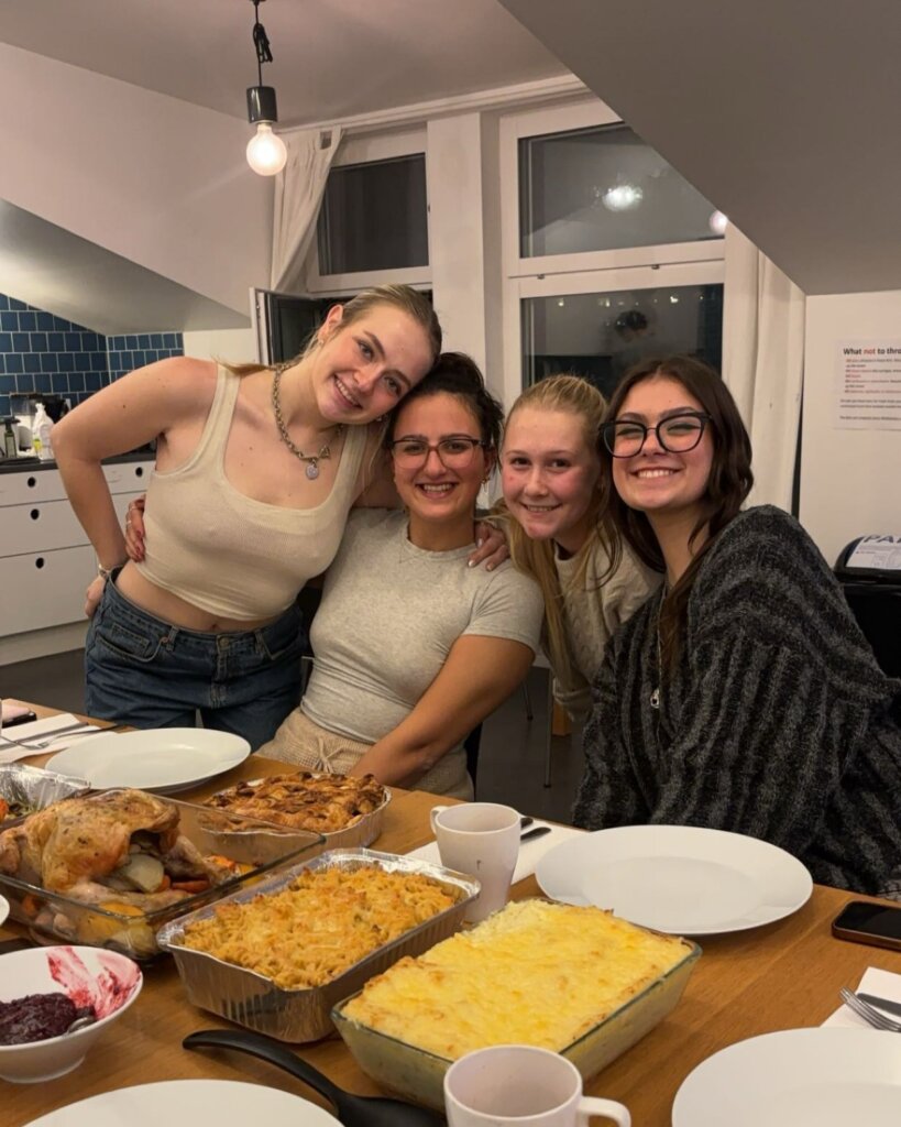Four friends gather for Friendsgiving in their residential building's kitchen with the food they prepared.