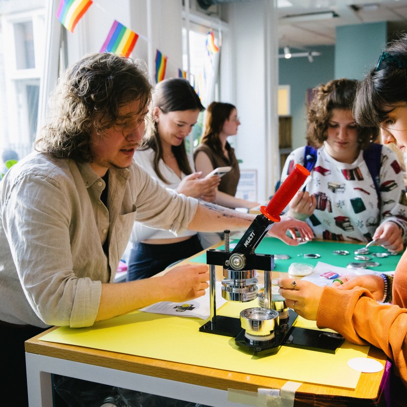 Devin engages with a student while tabling at the Activities Fair, showing how to use a button-making machine.